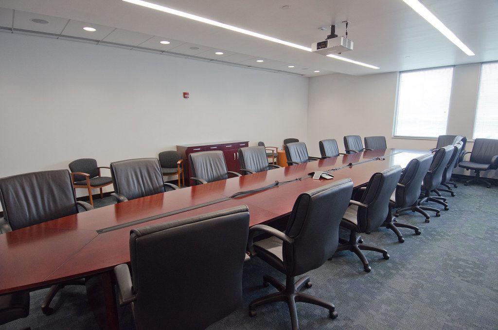An empty boardroom with a long wooden table and black leather chairs