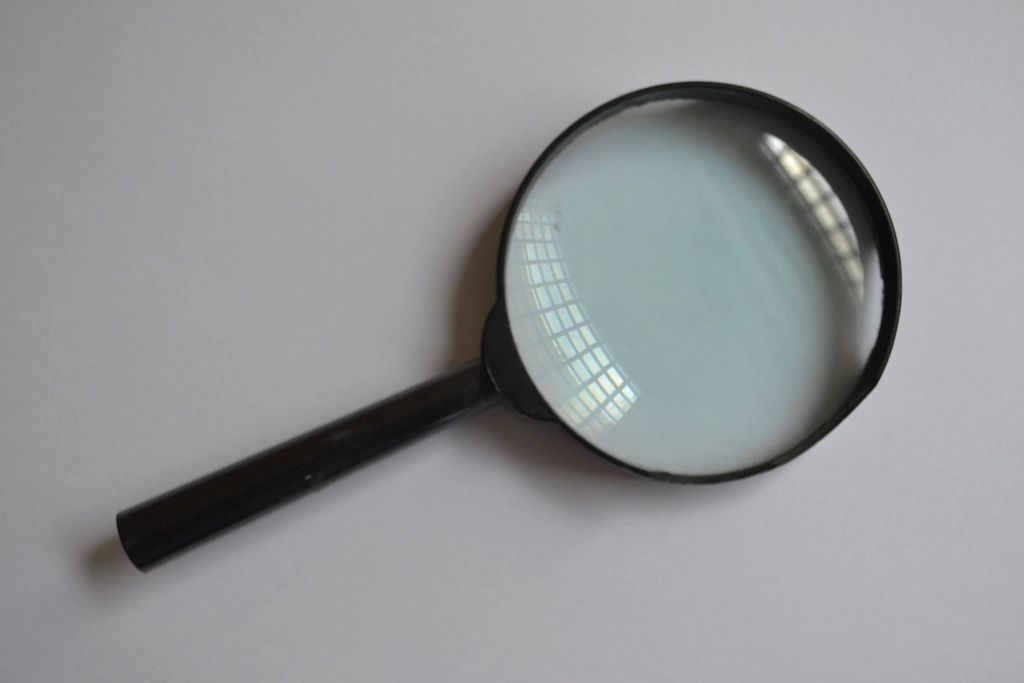 A black-handled magnifying glass lying on a pale grey surface