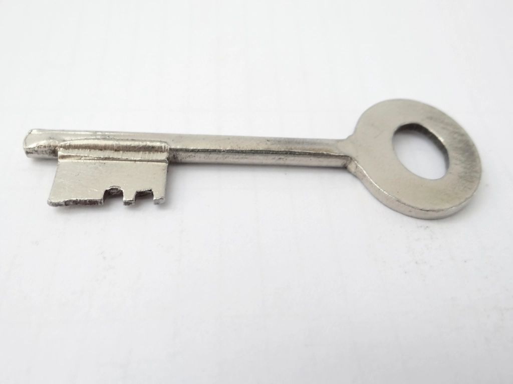 A plain metal door key lying on a white surface