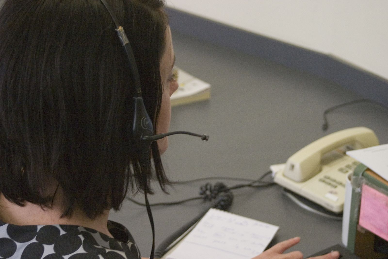 A person wearing a headset at a desk with a desk telephone, seen from behind