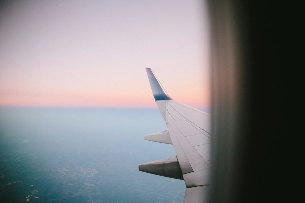An aircraft wing seen through a cabin window above the sea at dusk