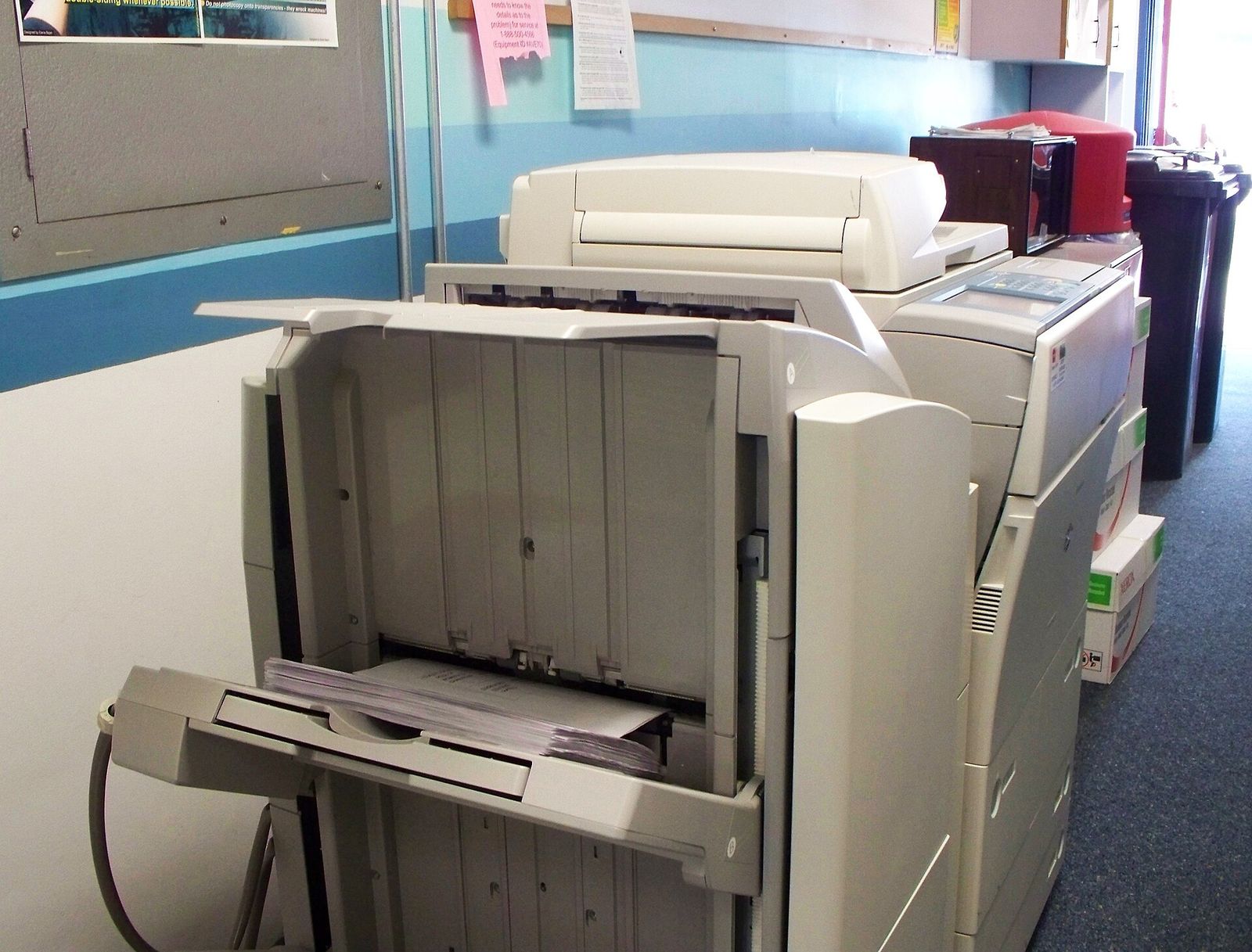 A large office photocopier with its side panel open in a corridor