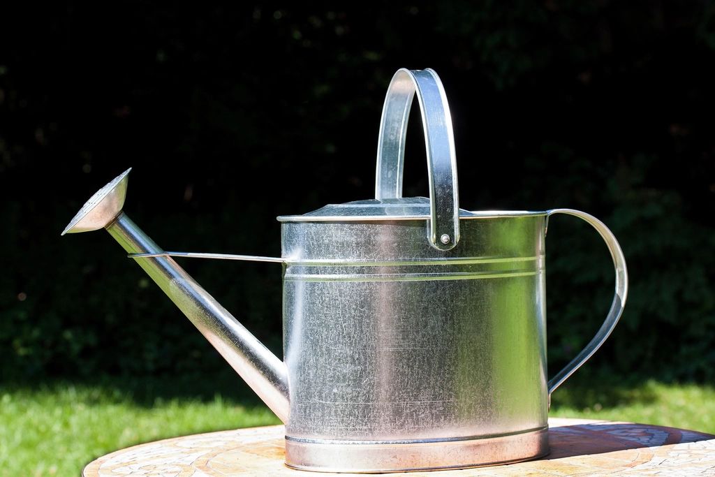 A galvanised watering can standing on a garden table in sunlight