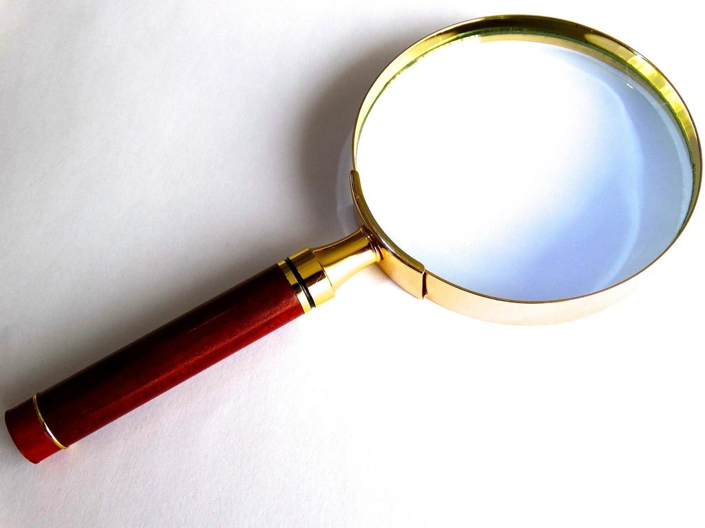 A brass magnifying glass with a red handle on white paper