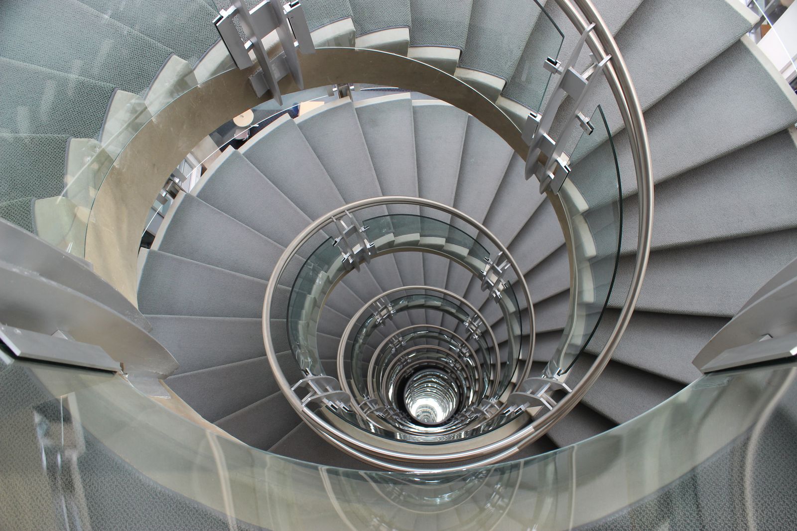 Looking down a modern spiral staircase with glass and steel rails