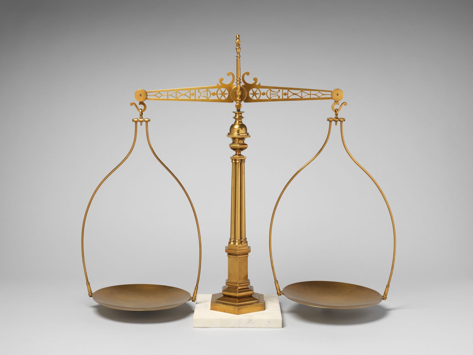 A brass balance scale with two empty pans on a marble base