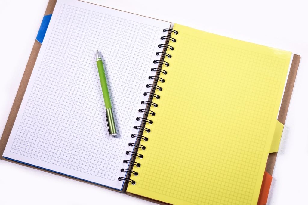 An open spiral notebook with squared paper and a green pen