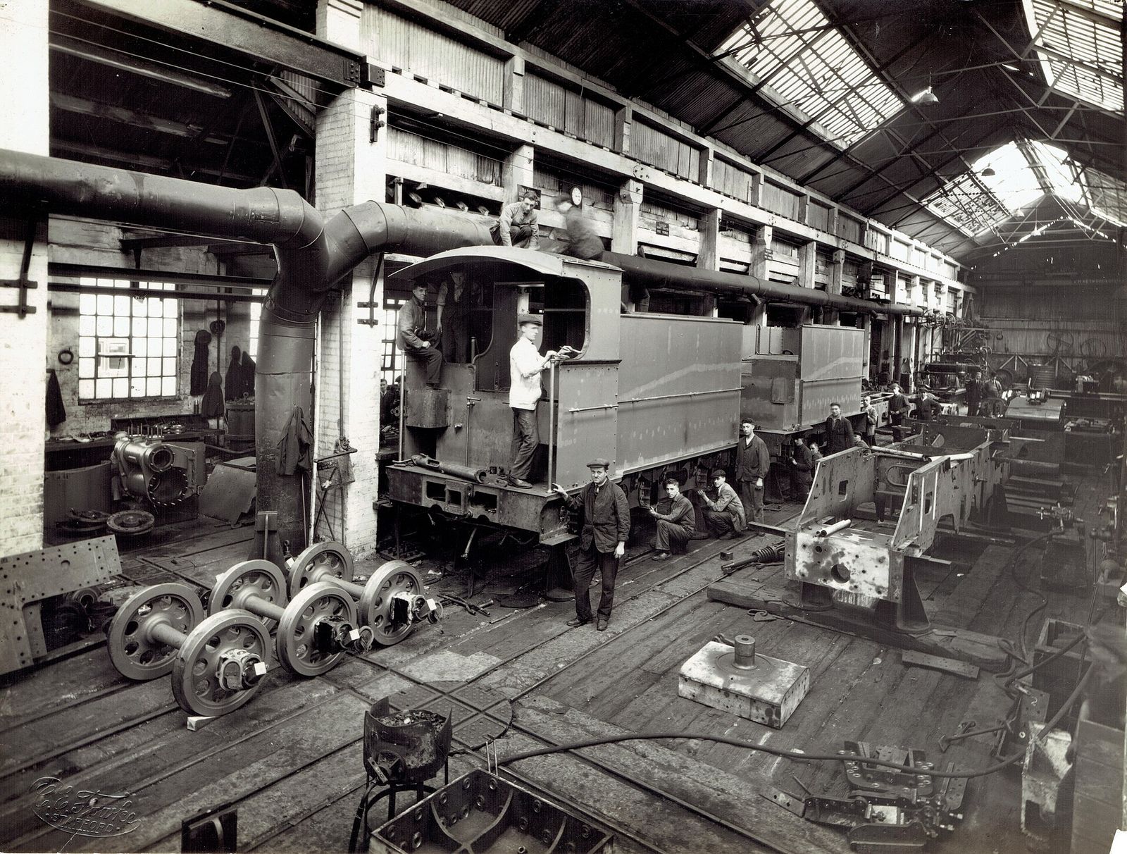 A historic black and white photograph of a steam locomotive workshop in western India