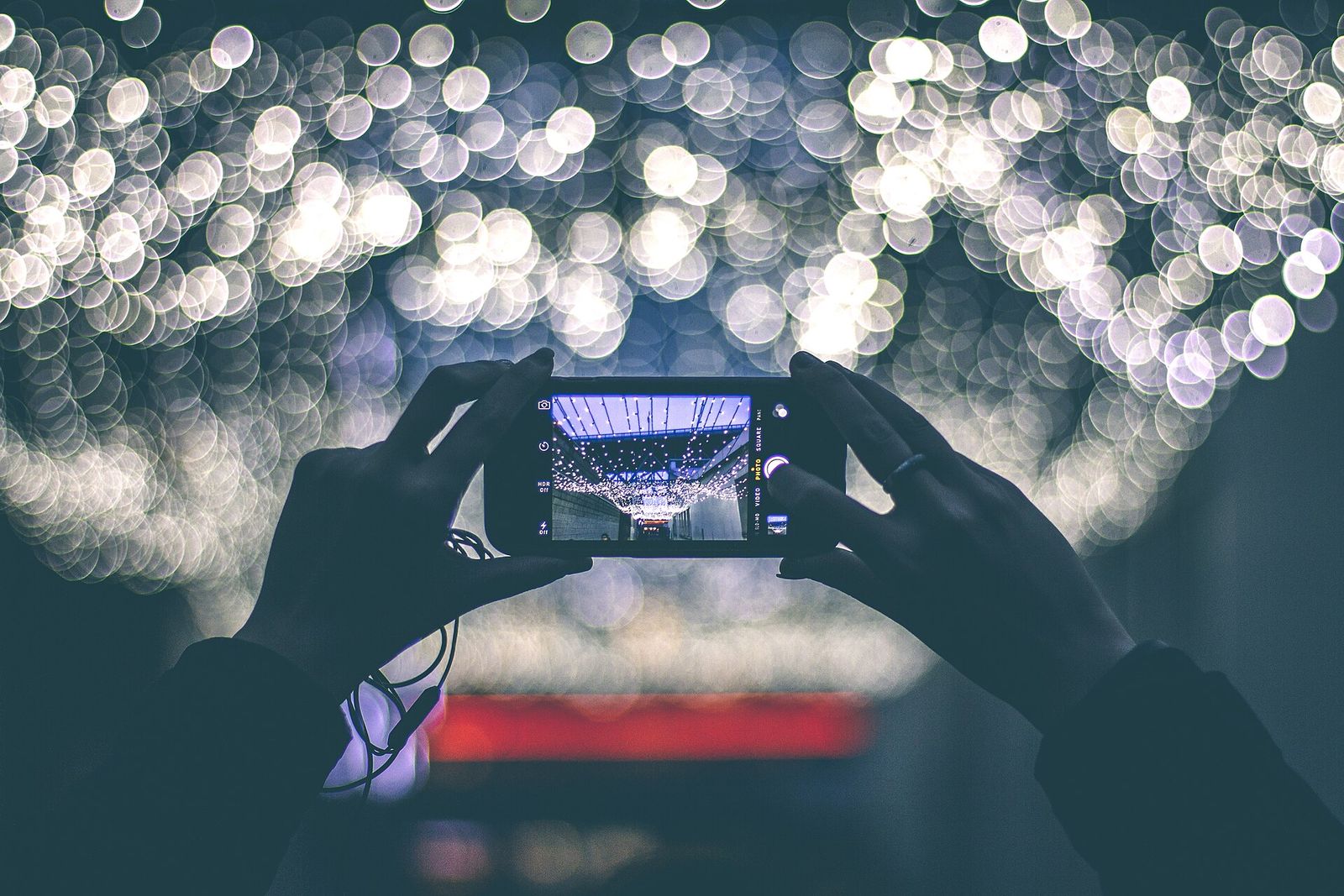 Two hands holding up a phone against a background of out-of-focus lights