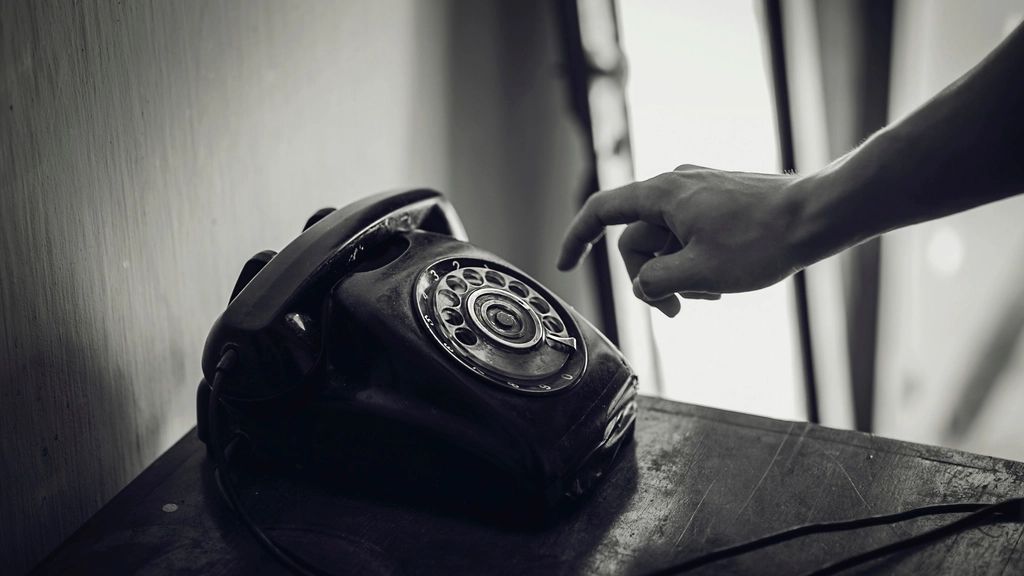 A hand reaching for an old rotary telephone, in black and white