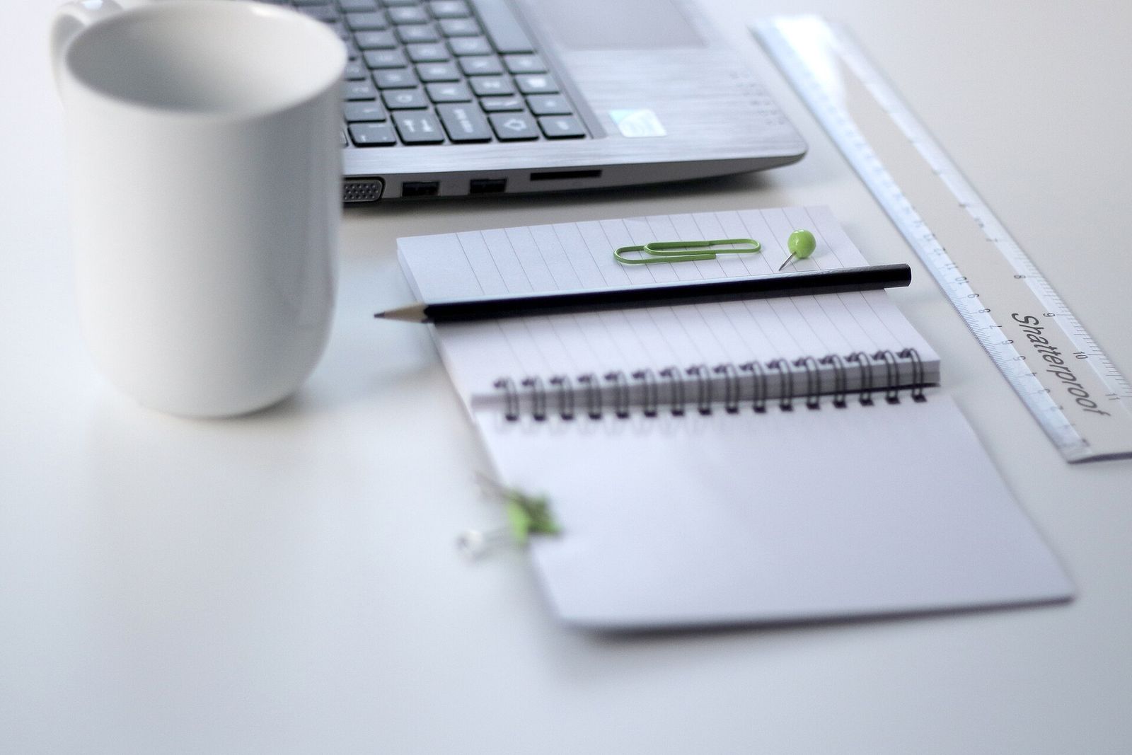 A notebook, pencil, ruler, mug and laptop on a white desk