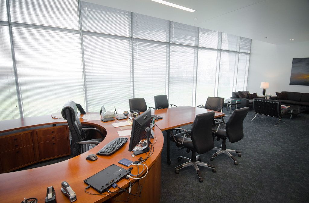 An empty office with a curved wooden desk, office chairs and a wall of windows