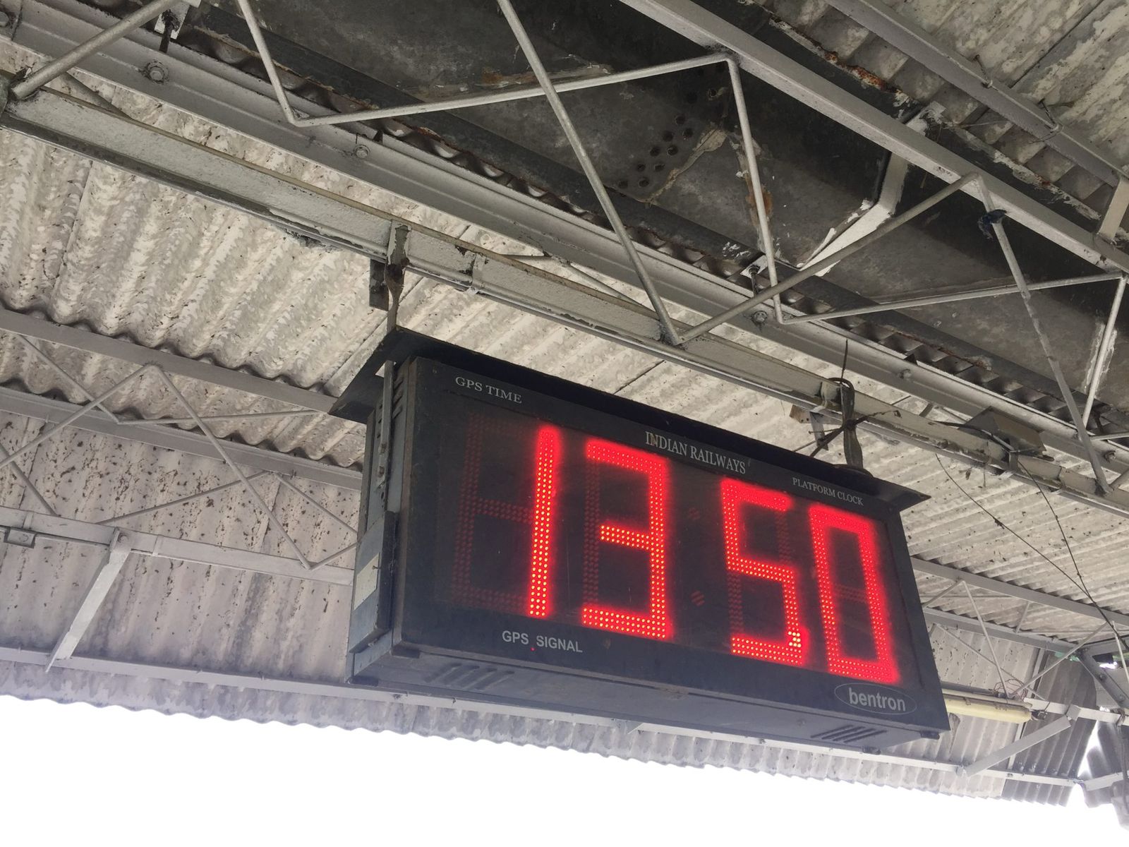 A digital clock hanging under the roof of an Indian railway platform
