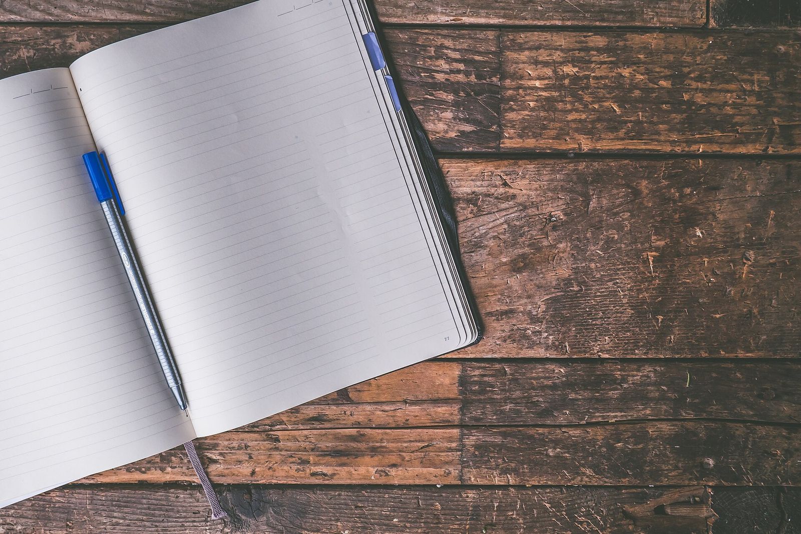 An open notebook with blank pages and a pen on a wooden table