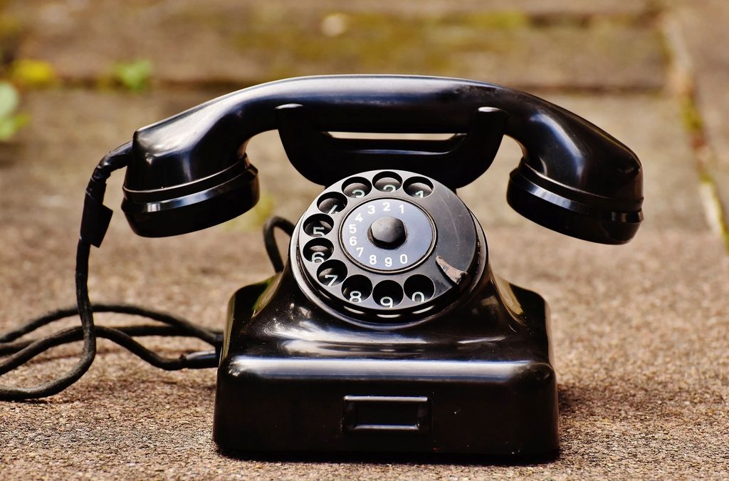 A black rotary dial telephone resting on a stone pavement