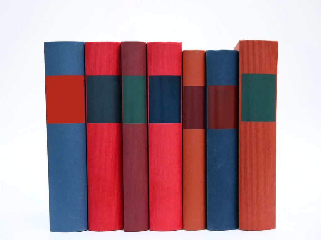 A row of seven hardbound book spines in blue, red and orange on a white background